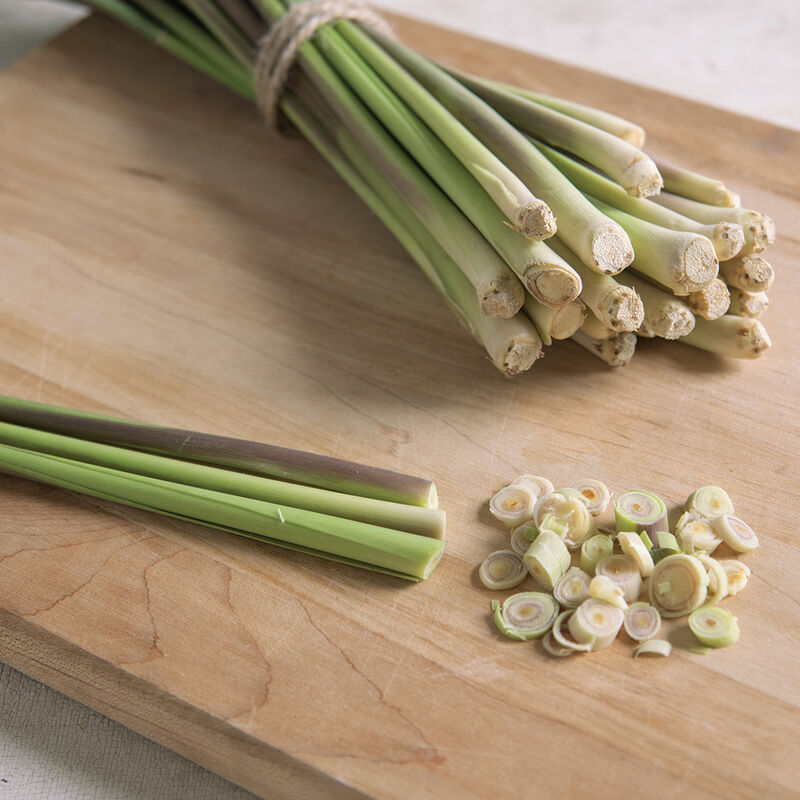 A bundle of lemongrass, whole and sliced, on a wooden cutting board.