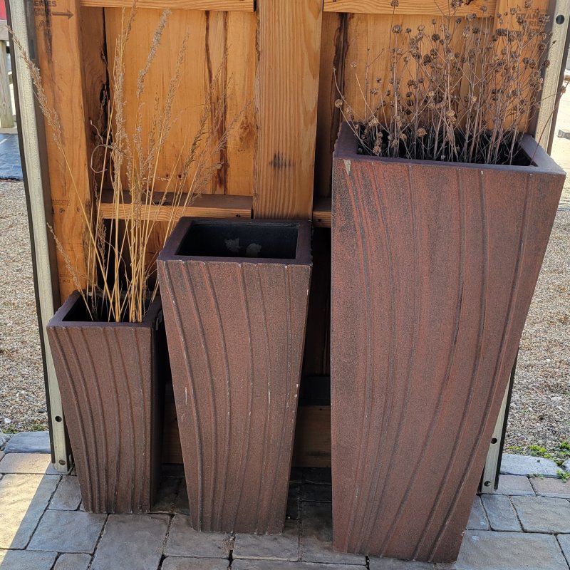 A trio of upright, square-shaped fiberglass Rio planters with sculpted natural curve elements; finished with a matte, brushed glaze in shades of charcoal gray and brick red.