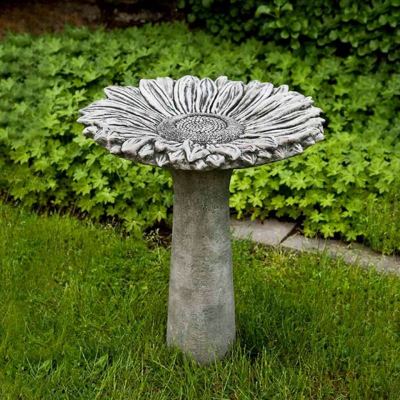A cast-stone free-standing birdbath in the shape and form of a large sunflower in bloom, placed in a garden environment.