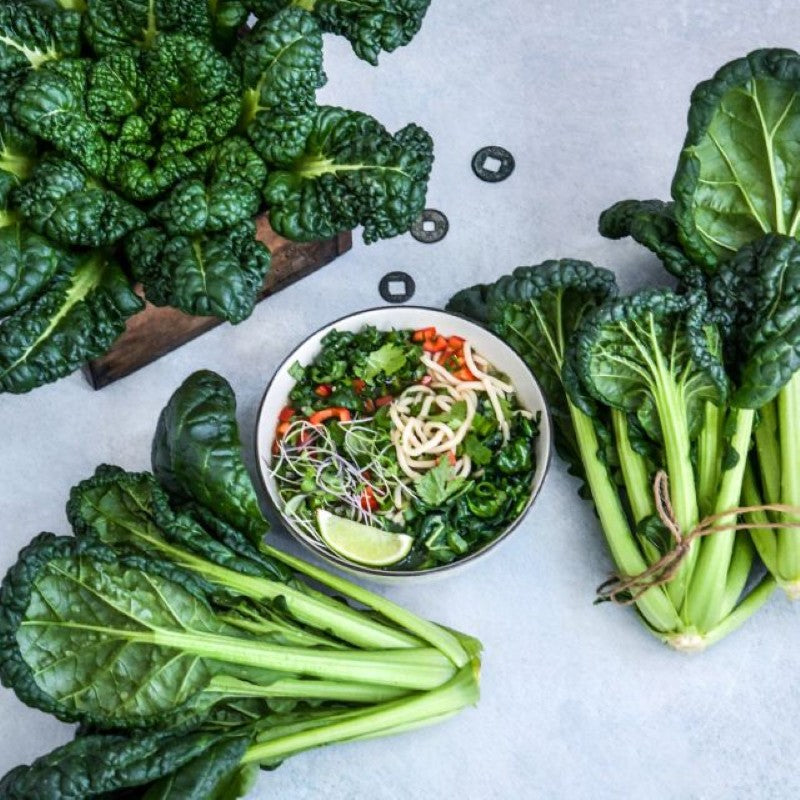 A photo of several bundles of chijimisai Asian cabbage with a bowl of Asian noodles in the center