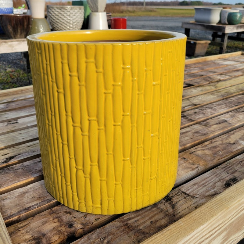 A straight-walled round planter with sculpted bamboo-forest texture on its exterior; finished with a bright yellow-green glaze.