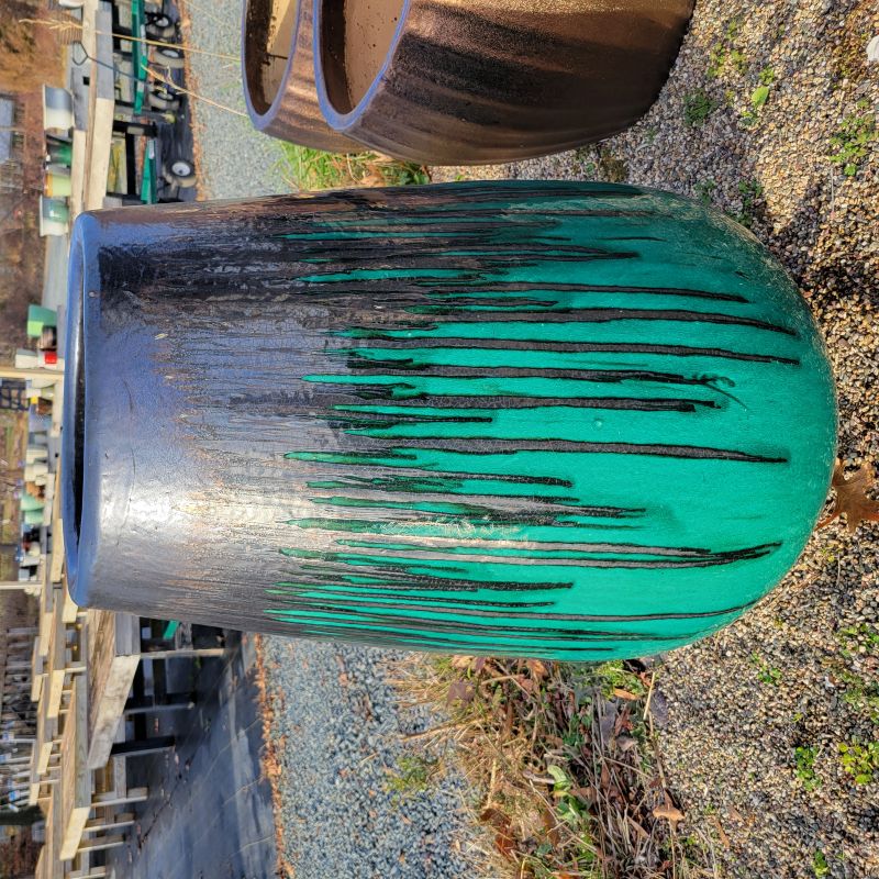 A large, upright, vase-like planter with a rounded shape and bowed walls; finished in a jade green and dark black-bronze drip glaze.