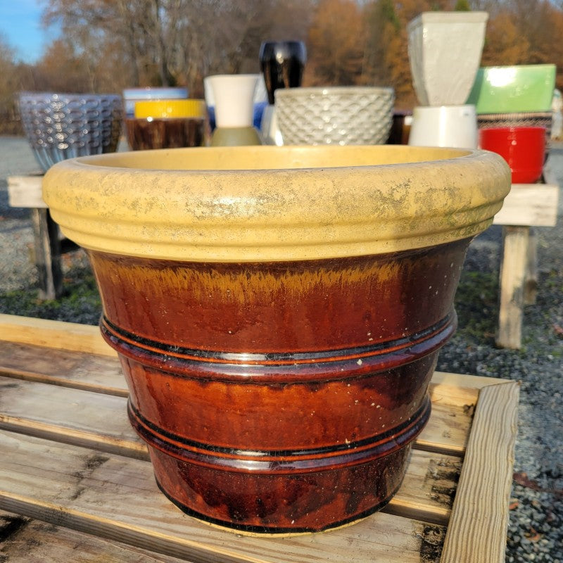 A large earthenware planter shaped like an inverted bell and finished with a with cola-brown glaze and cream-colored interior and lip.