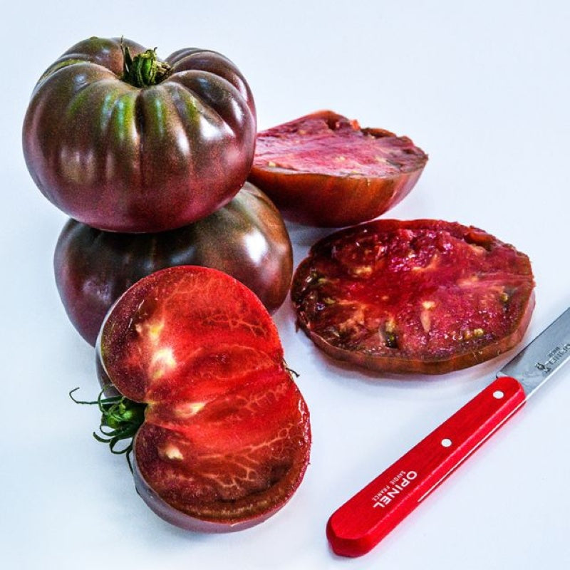 A small stack of large, purple-fleshed Black Brandywine heirloom tomatoes, whole and cut in half.