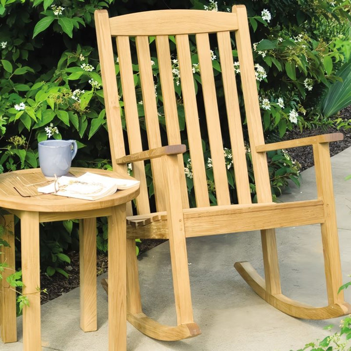 A Brittany Rocker chair placed alongside a Canterbury 20" Tall Round Side Table in a patio area.