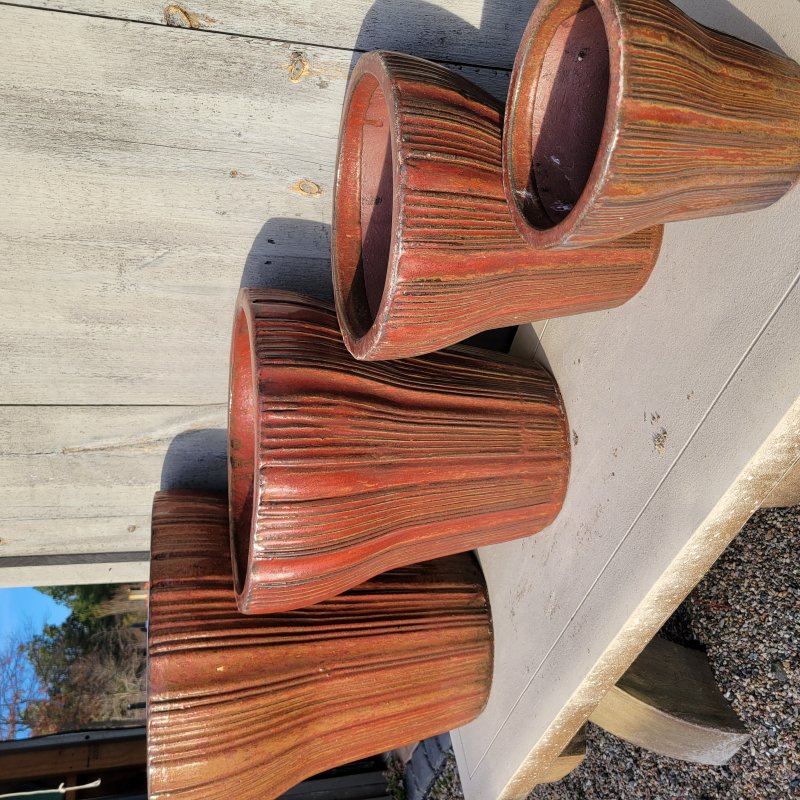 A group of Brush Creek planters, all flared in different sizes, with brick red/brown glaze and an irregular fluted design.