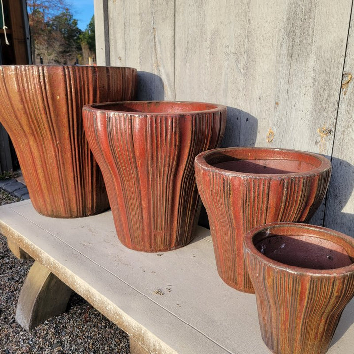 A group of Brush Creek planters, all flared in different sizes, with brick red/brown glaze and an irregular fluted design.