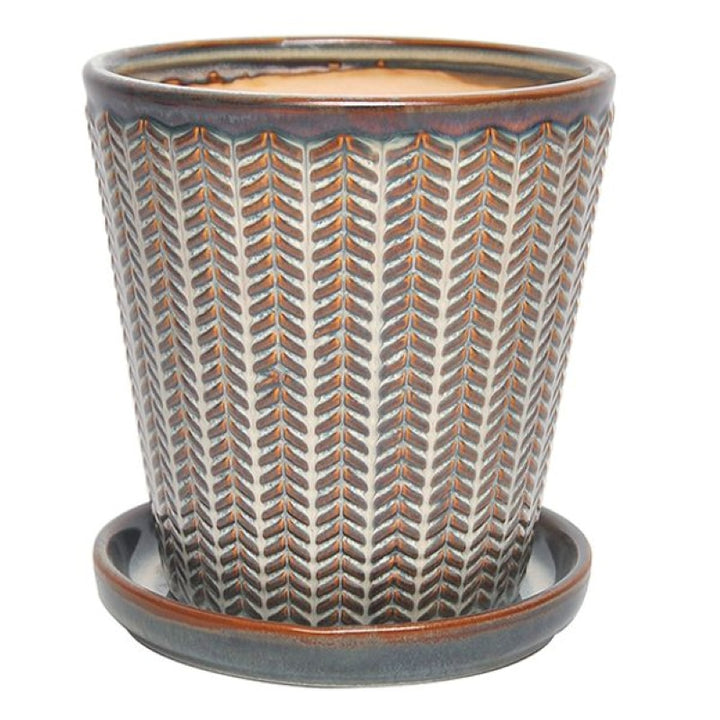 A stock photo of an upright rounded planter with angled walls and a built-in saucer; decorated with a carved chevron line design and finished with a cream white and brown glaze.