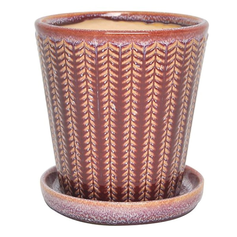 A stock photo of an upright rounded planter with angled walls and a built-in saucer; decorated with a carved chevron line design and finished with a brick red and white speckled glaze.