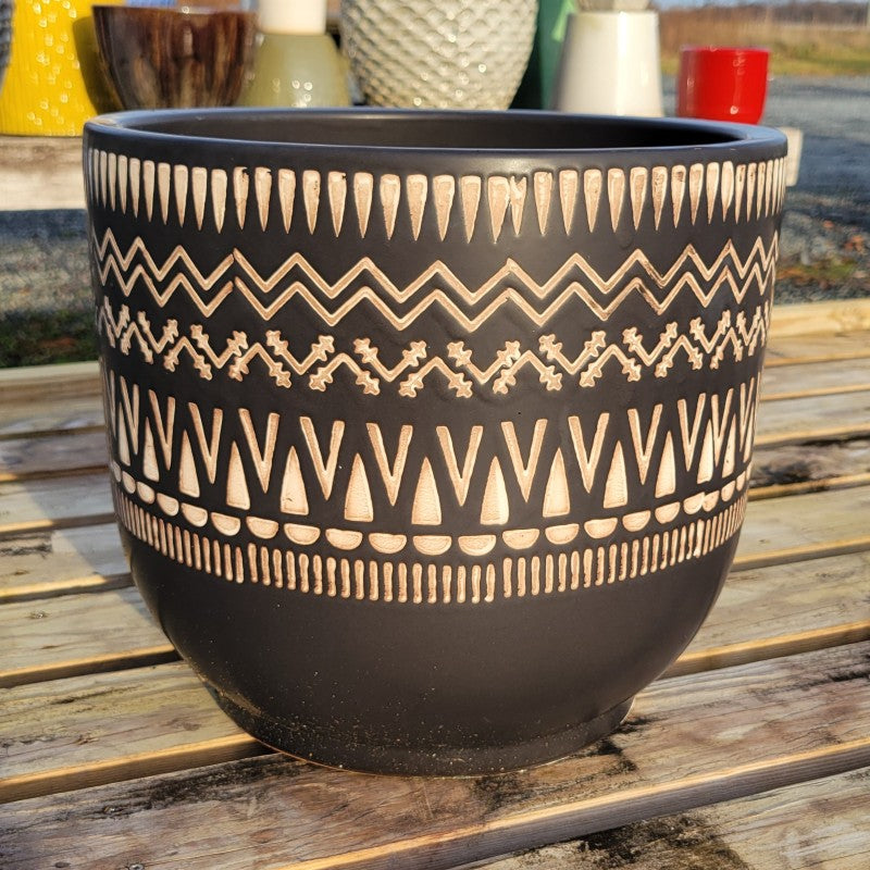 Rounded planter with straight walls and carved boho chevron design elements; finished with matte-black finish cream-white glaze.