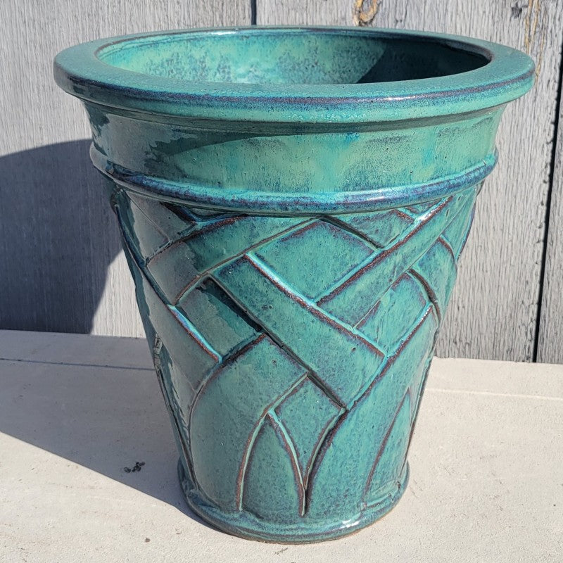 An upright, vase-like, rounded planter with sculpted woven pattern at the base, finished in a blue-green glaze over raw stoneware.