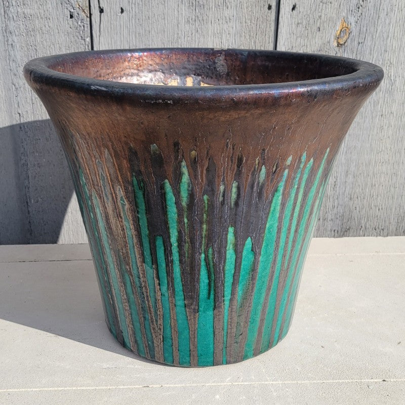 A plain, flared, rounded planter finished in a jade green and dark bronze drip glaze.