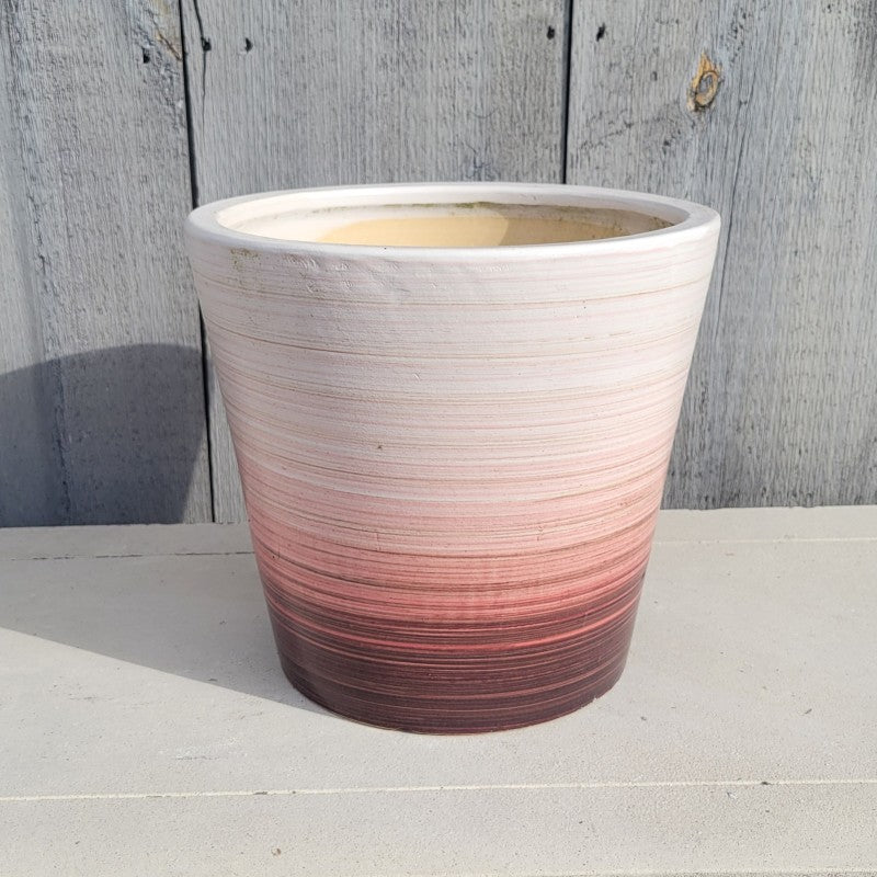 A rounded planter with a brushed, matte ombre glaze that fades from dark maroon-red at the base to sandy white at the lip.