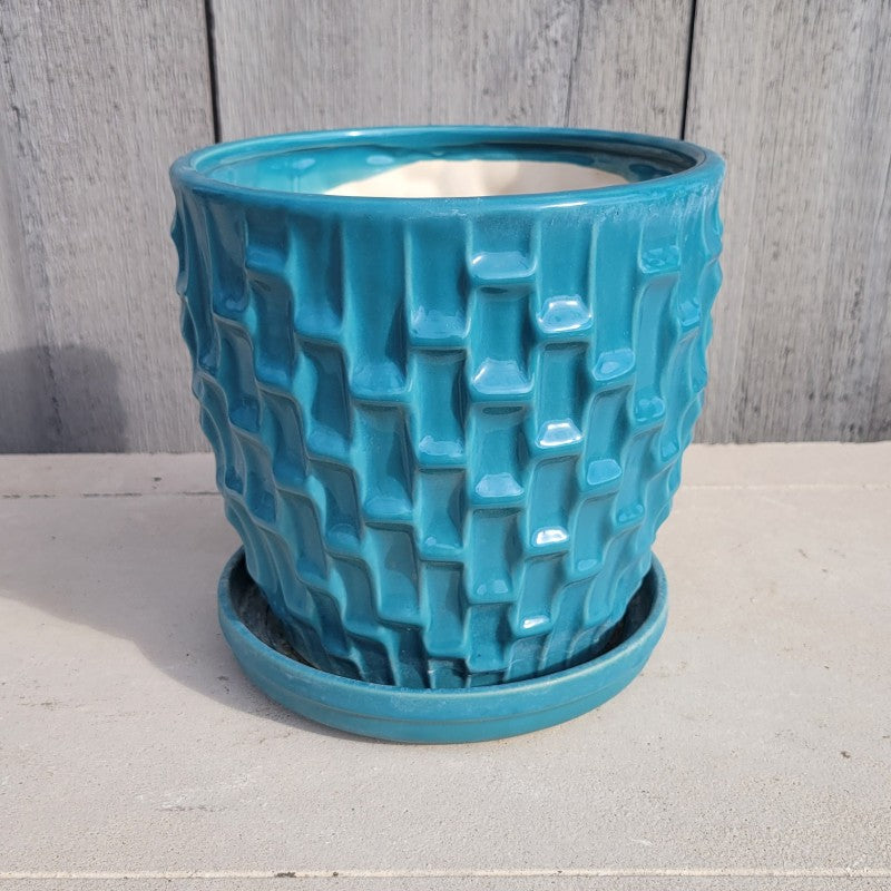 A round planter with built-in saucer and a sculpted geometric, shingle-like texture; finished in a teal blue glaze.