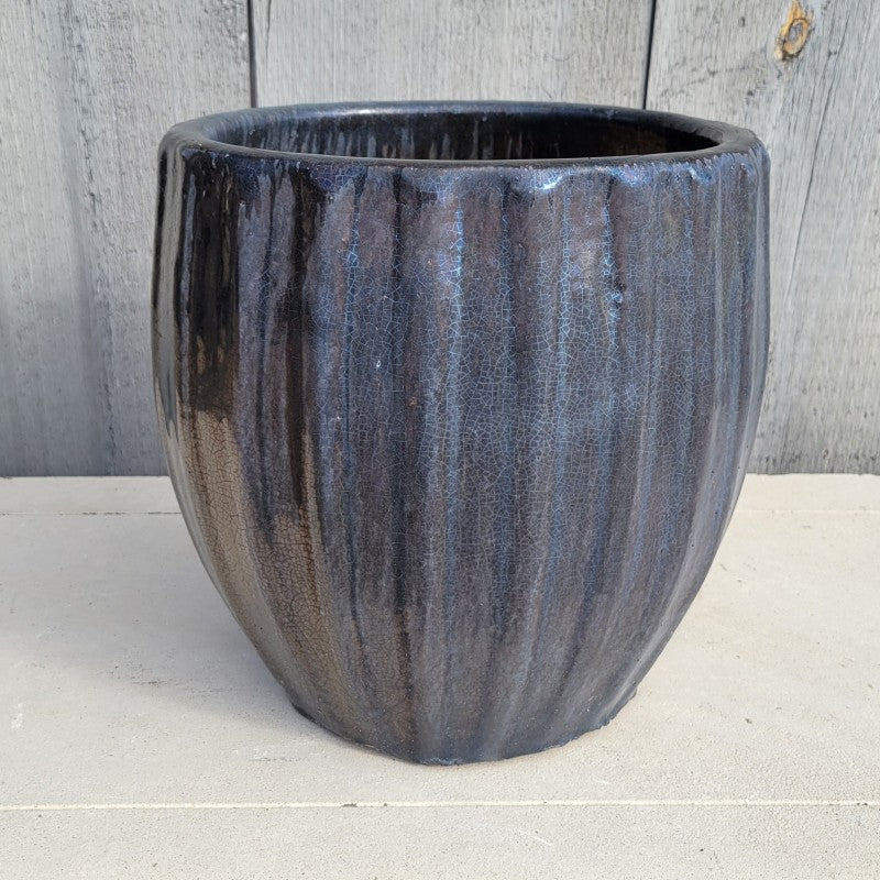 A rounded planter with bowed walls and a fluted appearance; finished in a metallic black and pearlescent blue glaze.