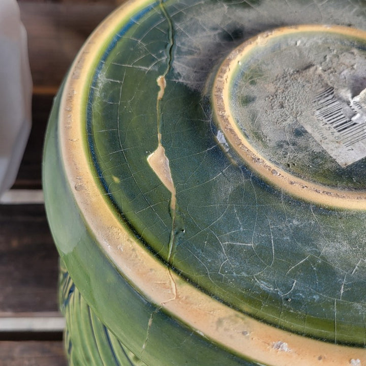 A photo illustrating an epoxy repaired crack on the bottom of the saucer section of a blue and green glazed Fan Planter.