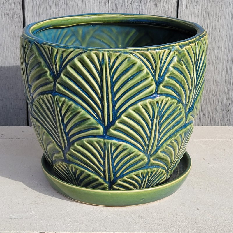 A rounded planter with built-in saucer; decorated with a sculpted fan/palm frond design with blue + green multi-color glaze.