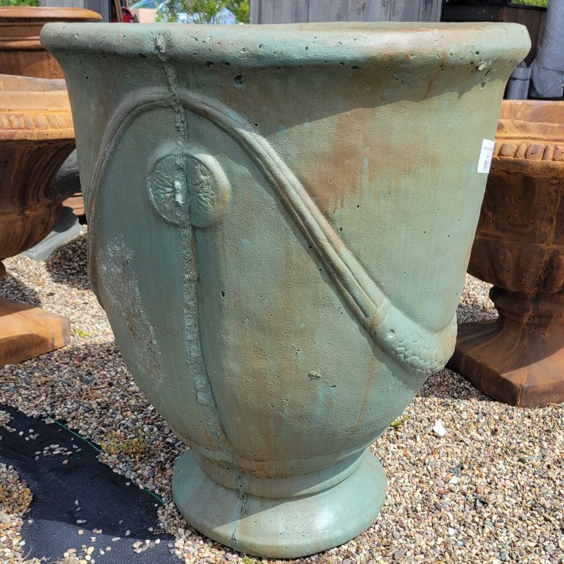 A close-up photo of a large, classically styled cast-stone planter with drapes and medallions, finished in Verdigris burnished green