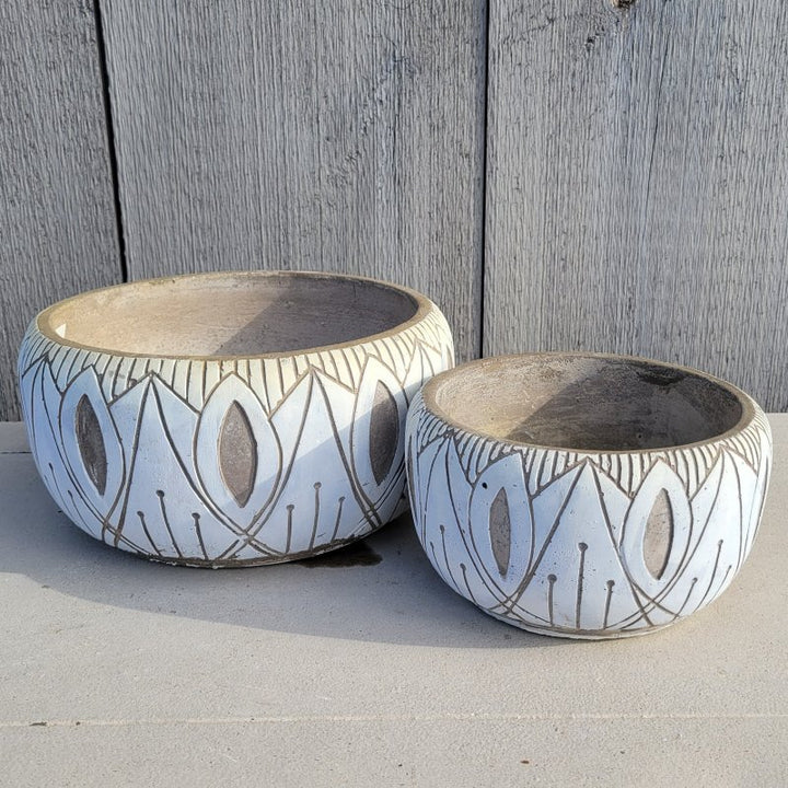 A pair of rounded, bowl-style planters with carved, abstract designs on the exterior; small and large planter are both finished in matte white glaze and raw earthenware.