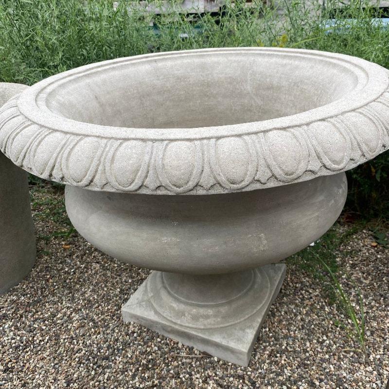 A large, round, cast-stone planter with a square base and an egg and dart pattern around its prominent rolled rim.