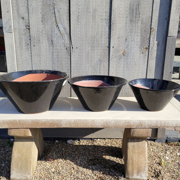 A set of Low Flared Basin planters, ranging from large to small moving from the left to the right; all planters are finished in glossy black glaze.