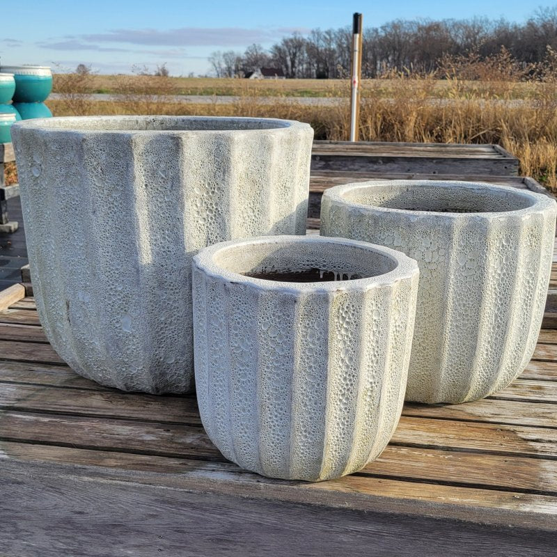 A trio of small, medium, and large Maris planters, rounded in shape with straight walls, fluting around the edges, and a rough, coral textured glaze.