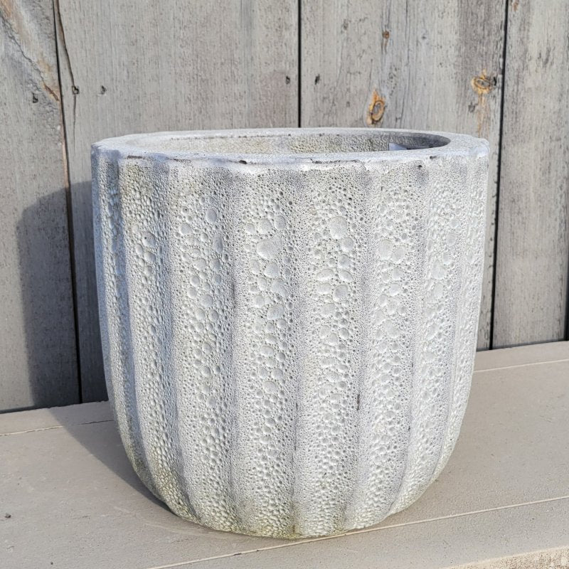 A rounded Maris planter with straight walls, decorated with a fluted design around its exterior; finished with a rough coral/pumice-stone glaze in gray-white.