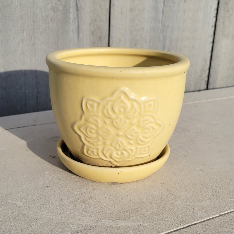 A small rounded planter with built-in saucer; the side facing the camera is decorated with mandala-style medallion element, and the planter is finished with a pastel daffodil yellow glaze.