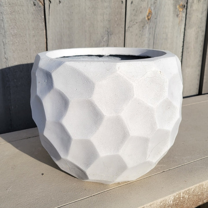 A rounded fiberglass planter with a faceted, gem-stone like appearance; finished in a matte, bone-white glaze.