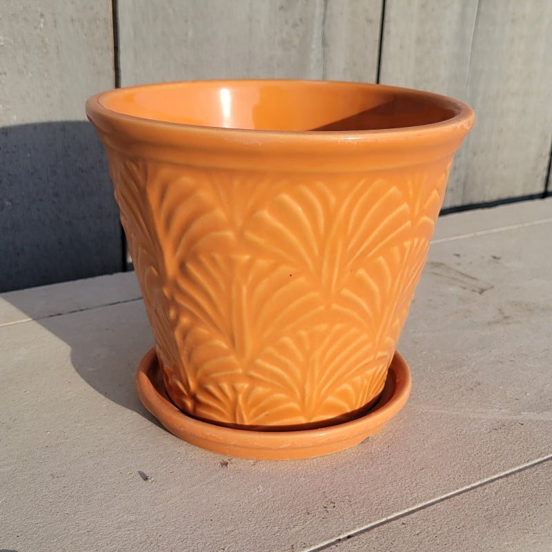 A vase-like Nouveau planter covered in palm frond designs and finished in a bright orange glaze.