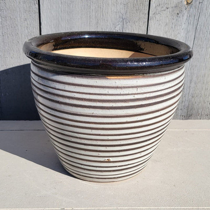 A round, flared low kettle pot planter with a pronounced lip; decorated with carved and glazed pinstripe design in white and black.