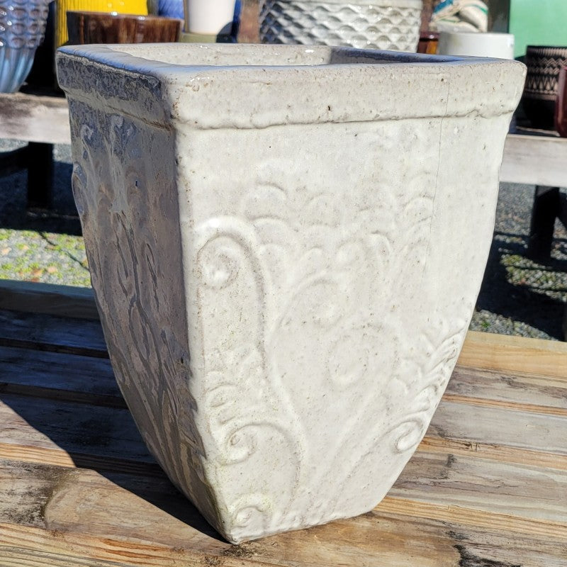 An upright square planter with bowed walls and a sculpted botanical design; finished with a cream-white glaze.