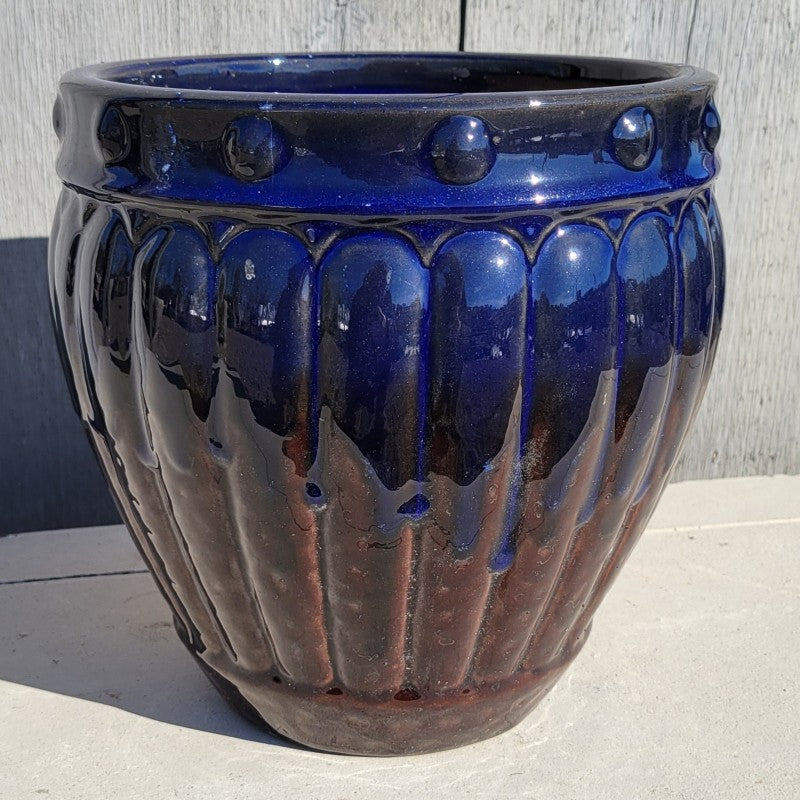 An ornate, rounded Prestwick planter with bowed walls and a sculpted ridge and dot design; finished with dark brown to midnight blue drip glaze.