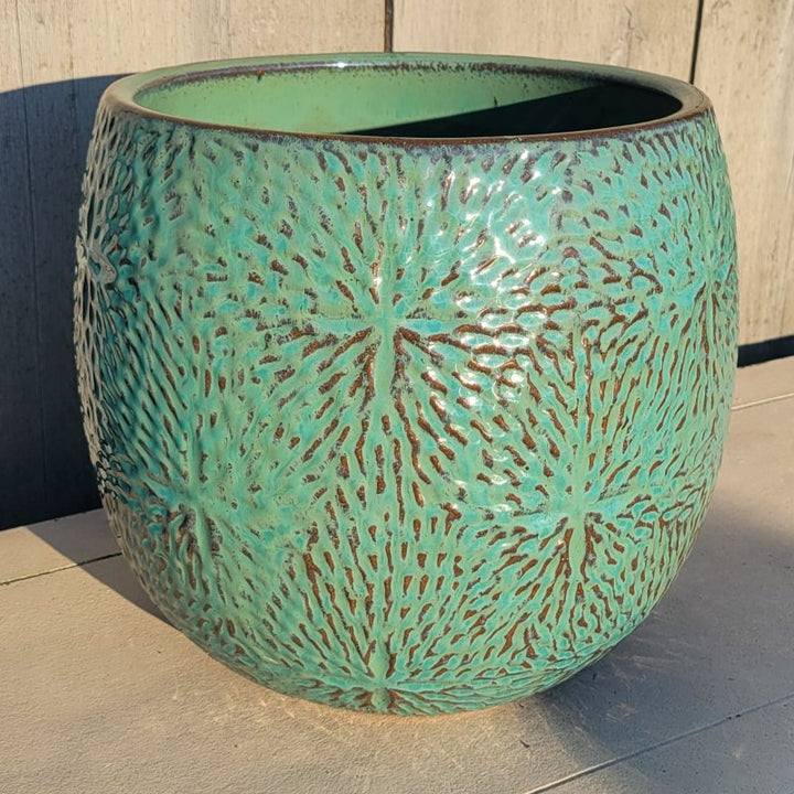 A rounded Sand Dollar Planter with bowed walls, and carved sand dollar designs; finished in a turquoise/sea-foam green glaze with raw stoneware accents.