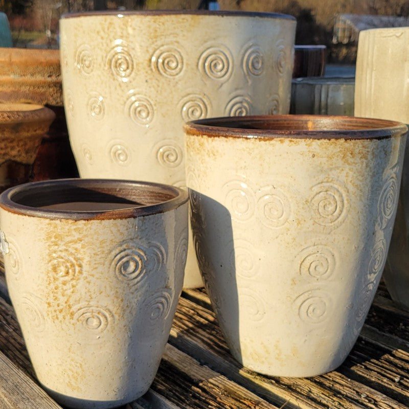 An upright, rounded, egg-cup style planter with a carved swirl pattern; finished in a brown-accented cream-white glaze.