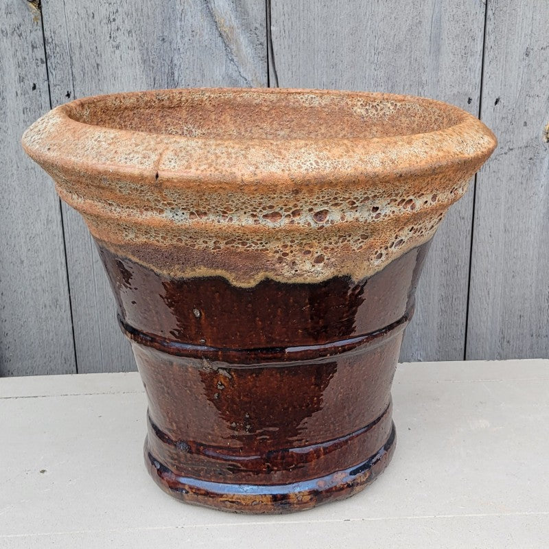 An open, rounded planter with a trumpet bell shape and sculpted ridges around the base, mid-section, and lip. Finished with a dark brown and rough-texture tan glaze.