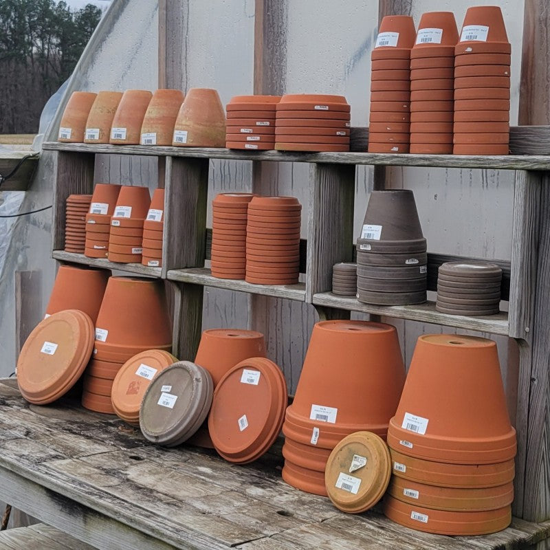 An assortment of red and dark gray terracotta saucers and planters.