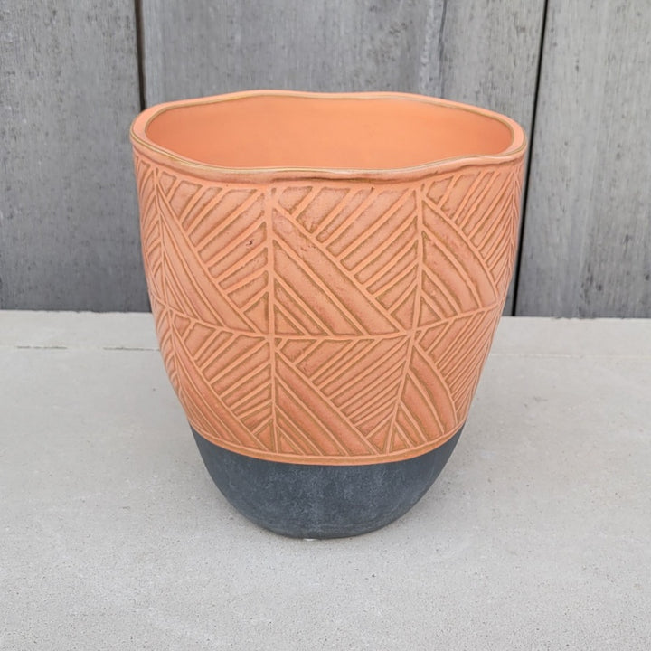 An upright rounded Tikal Planter with removable drainage plug and sculpted geometric line design; finished with a coral pink/orange and gray glaze.