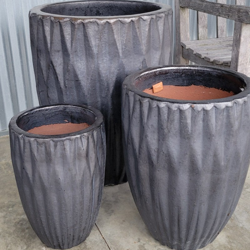 A trio of narrow rounded Tortona planters with sculpted diamond texture and a metallic, graphite-gray glaze.