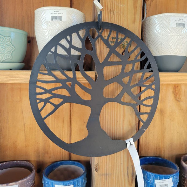 A black, powder coated Tree of Life hanging metal decoration hanging next to some pottery.