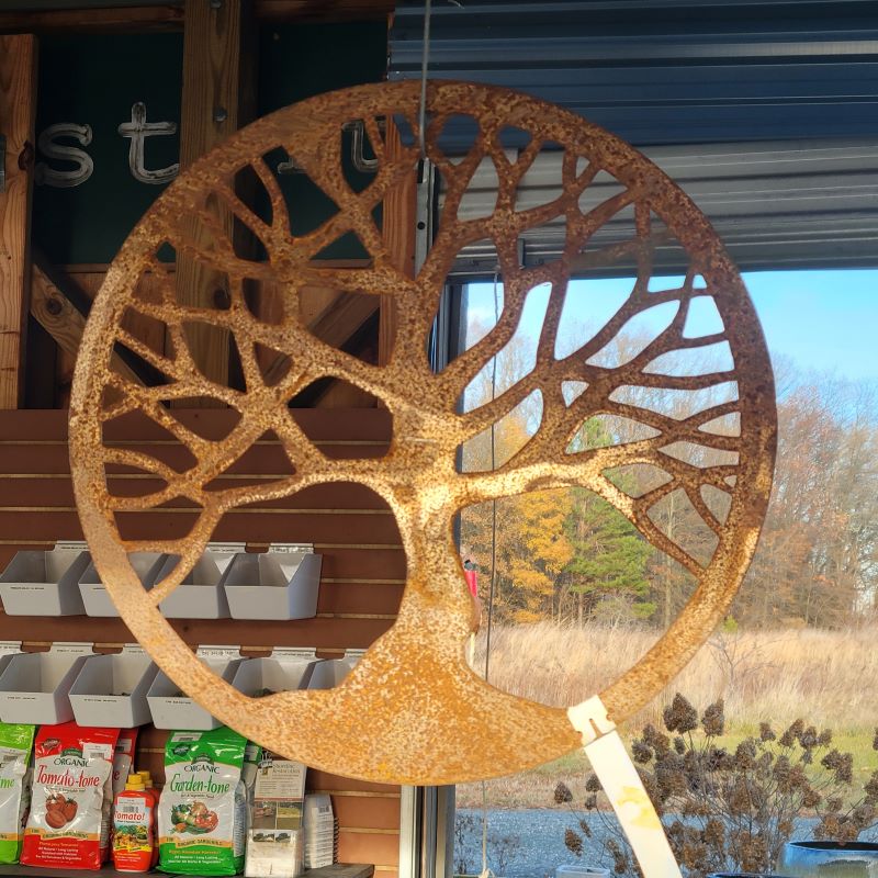 A raw steel finish Tree of Life hanging metal decoration hanging next to some pottery.