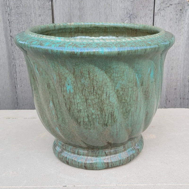 A rounded planter with pronounced base and rim, decorated with a sculpted spiraling wave design. Finished in a sea-foam and darker jade green 'Glacier' glaze.