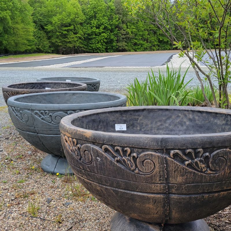 A photo of four large, bowl-shaped cast stone planters with a wave design.