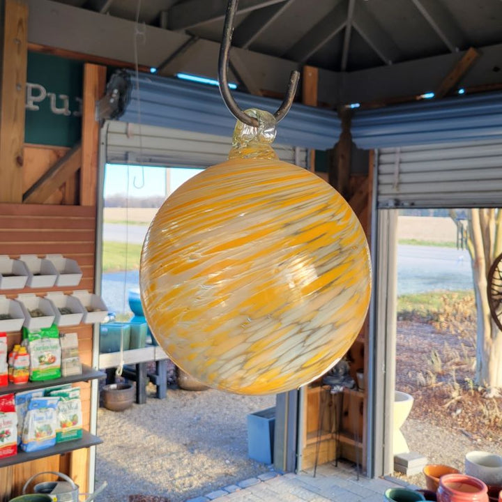 A small hanging witch ball decoration, made of clear glass with swirls of white and creamy orange speckles.